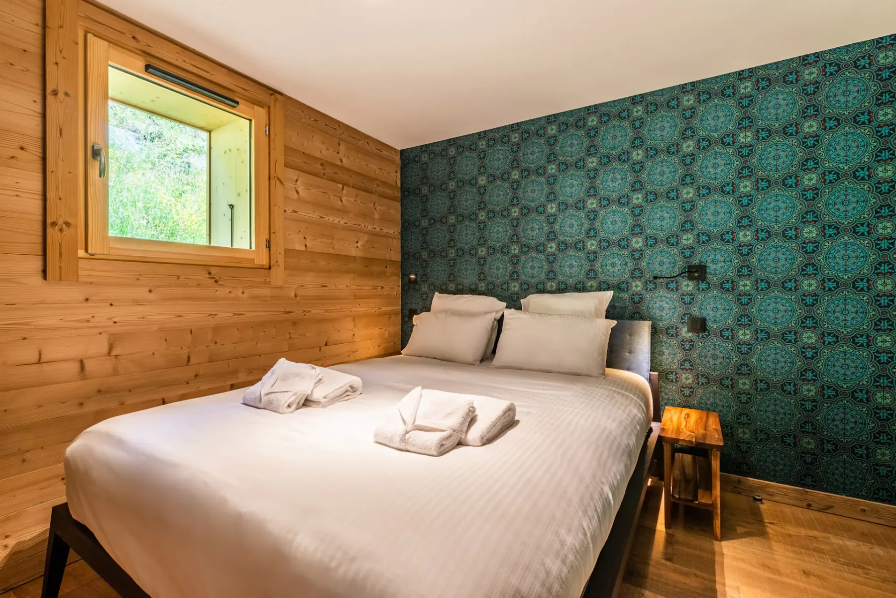 A bedroom with a neatly made bed, wood-paneled walls, and patterned wallpaper.