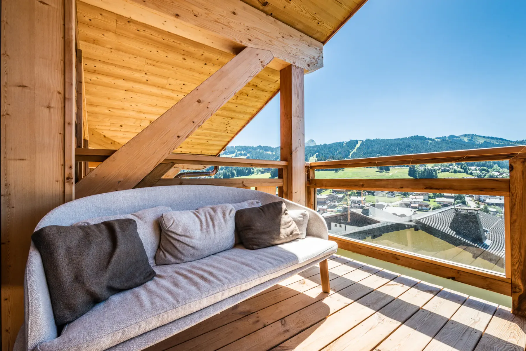 A covered wooden balcony has cushioned seating and a view of the surrounding mountains.