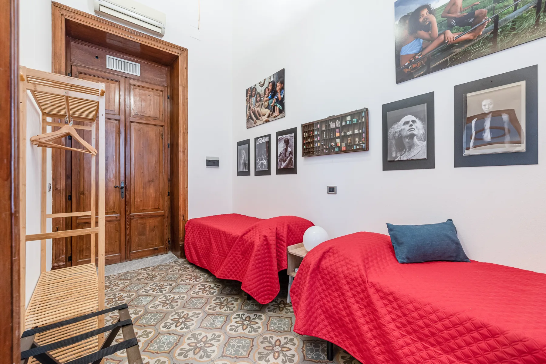 A bedroom with red-covered beds and framed pictures on the wall.