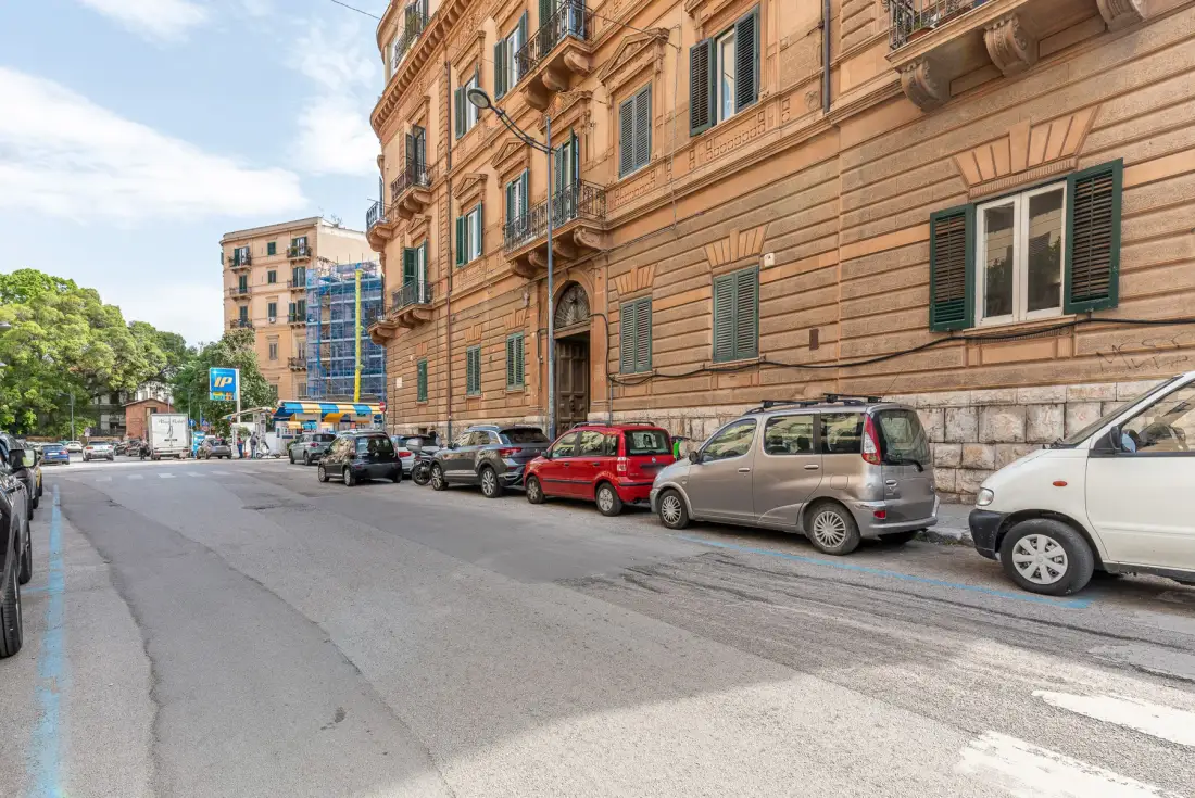 A city street lined with parked cars beside a large brick building.