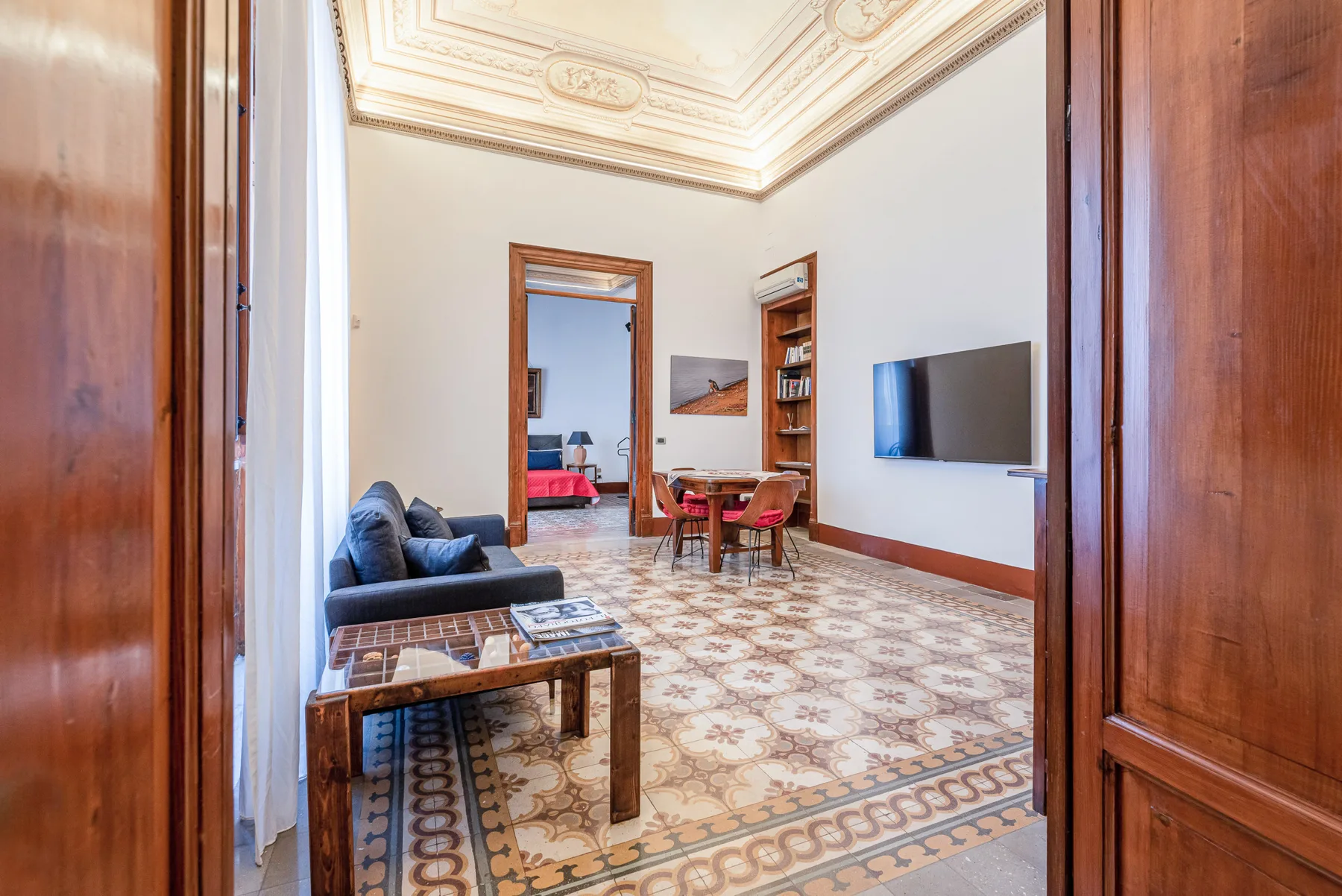 A sitting room with patterned tile flooring and a wall-mounted television.