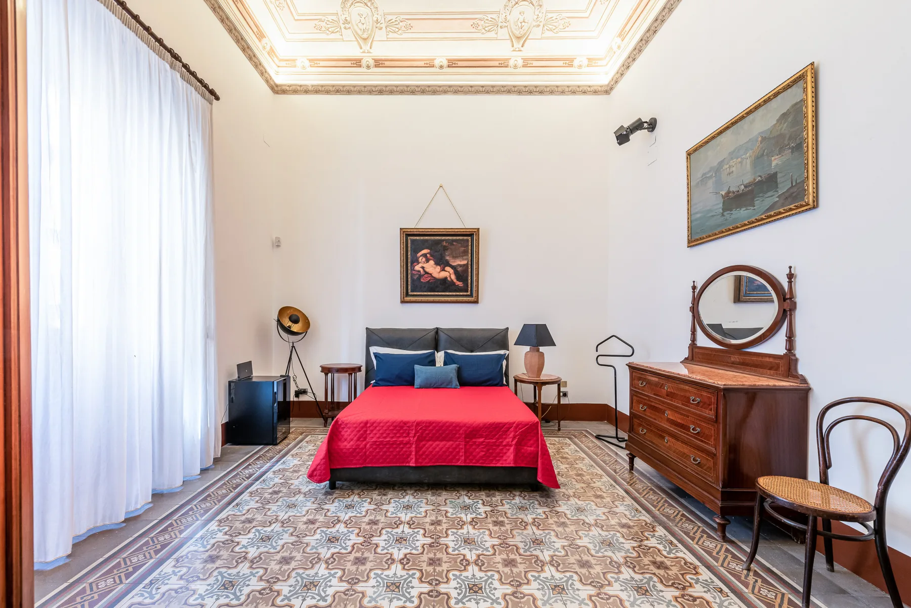 A bedroom with a bed, a dresser, and tall curtained windows.