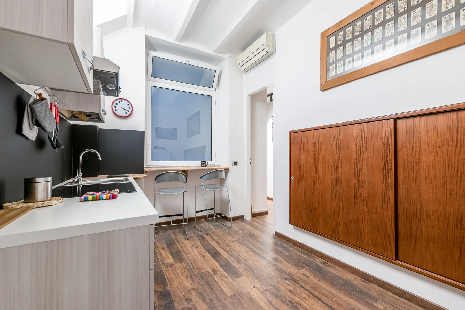 A compact kitchen and dining area with a counter, stools, and wood flooring.