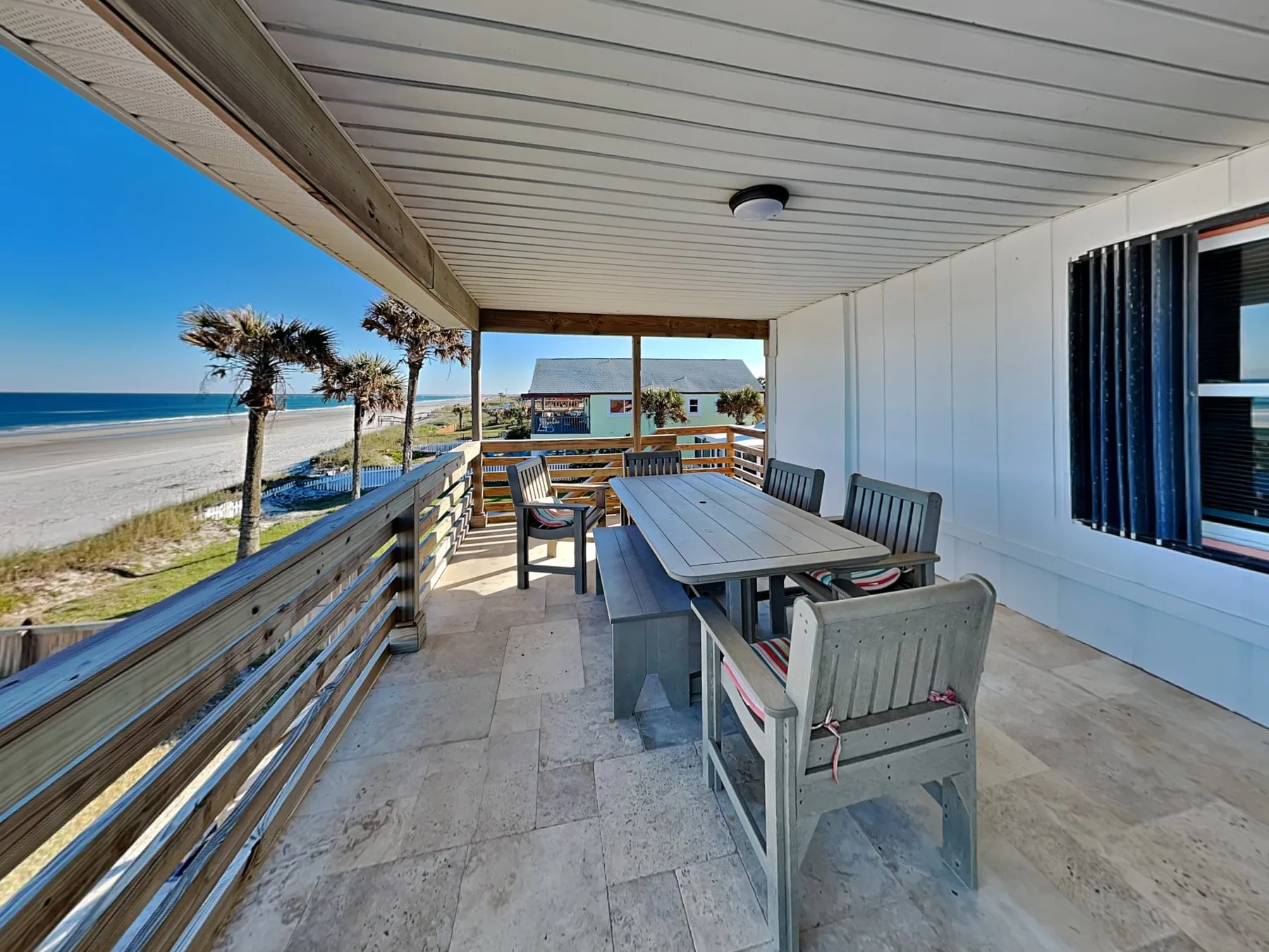 A covered seaside patio with outdoor seating and a view of the beach.