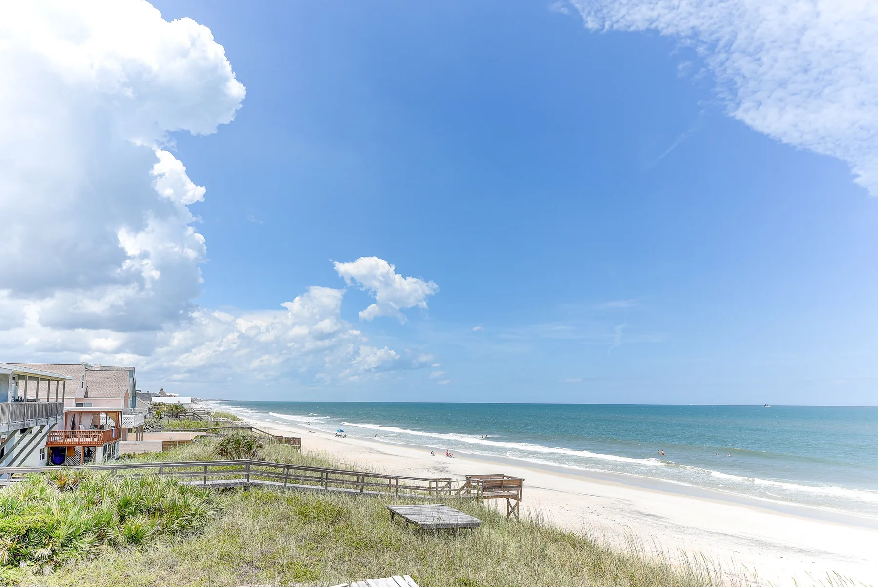 A sandy beach and ocean stretch beside grassy dunes under a partly cloudy sky.