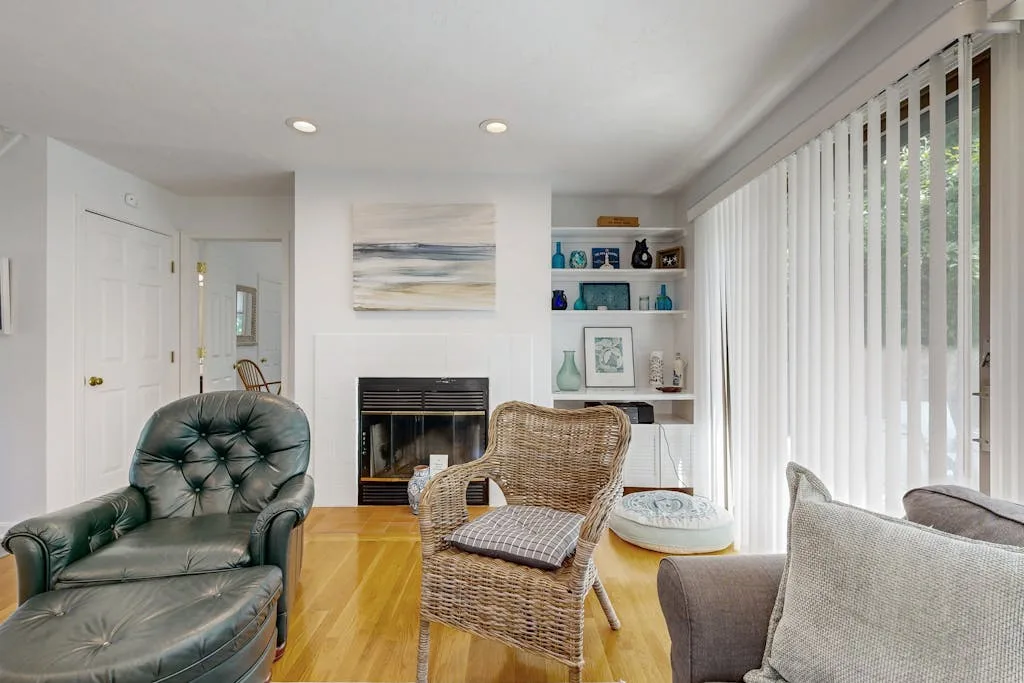A bright living room with seating, a fireplace, and vertical blinds.
