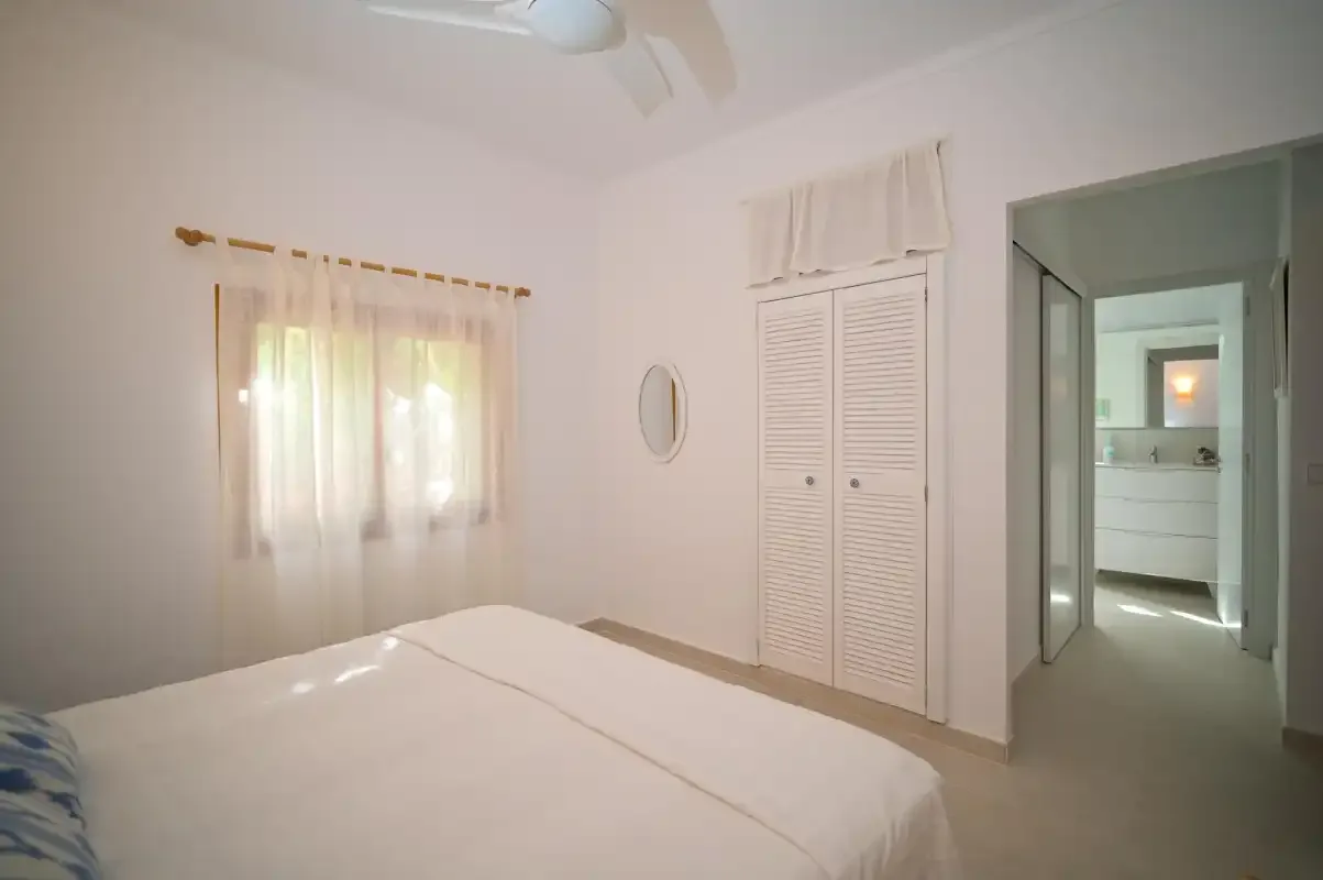 A bedroom with a bed, curtained window, and doorway to another room.