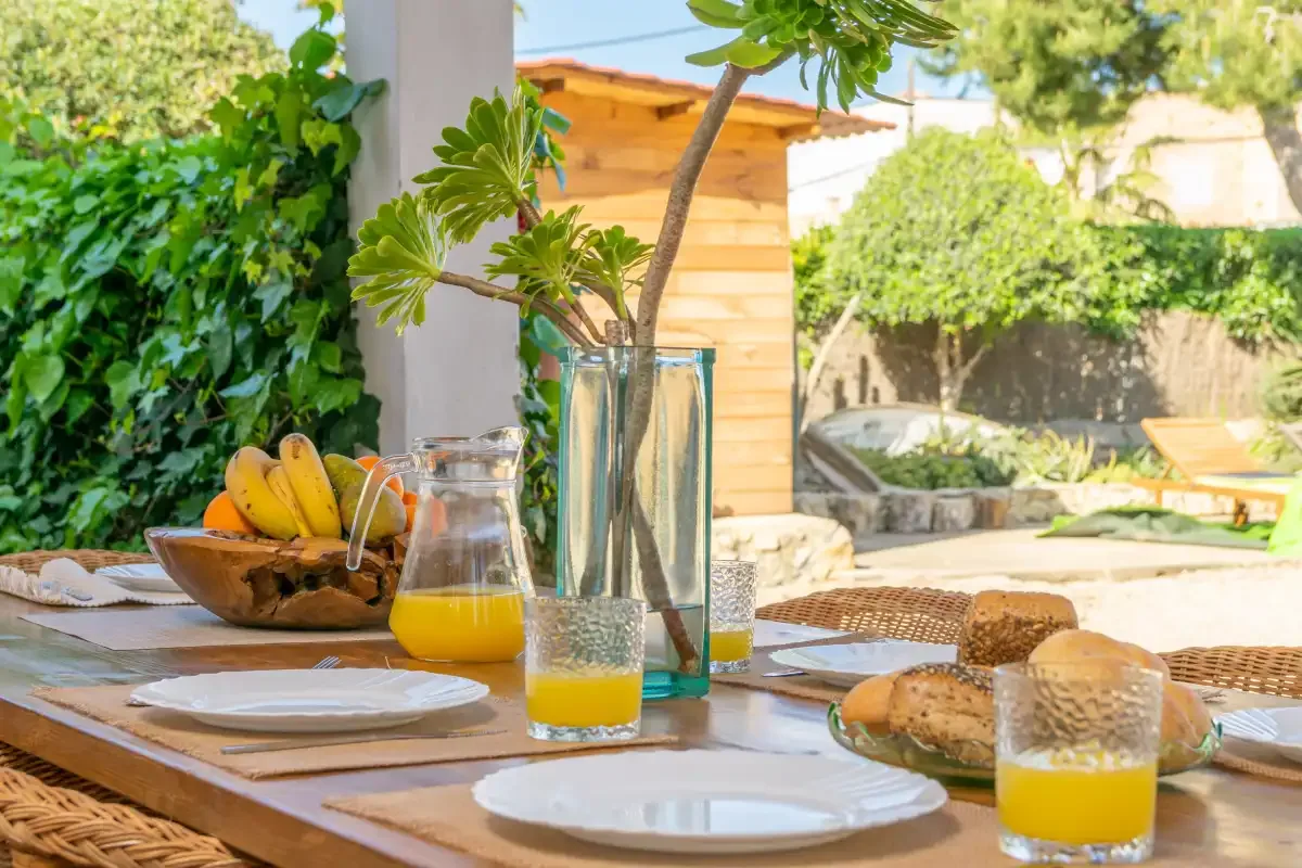 An outdoor dining table is set with plates, bread, and orange juice.