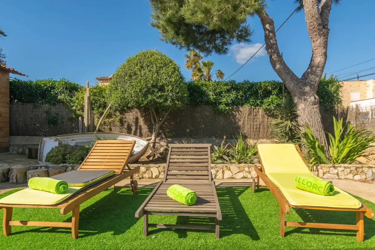 A sunny outdoor patio has lounge seating, green turf, and leafy plants.