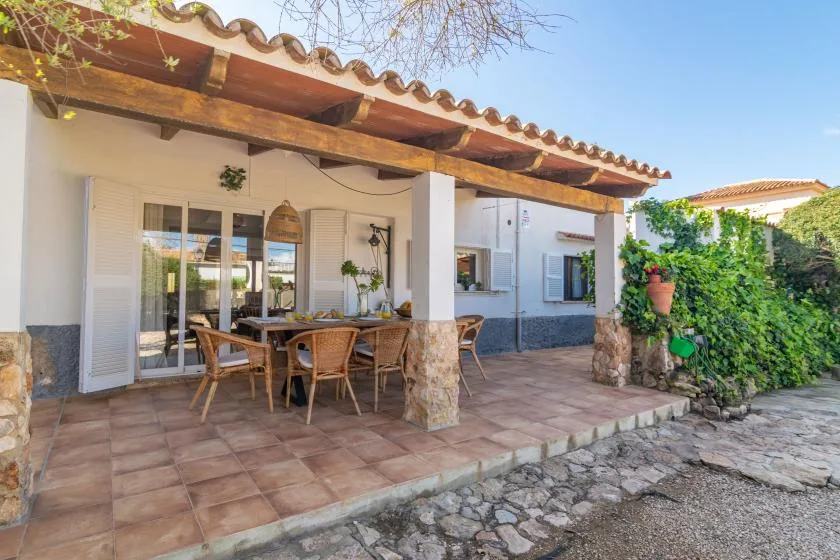 A covered outdoor patio with a dining table and seating beside the house.