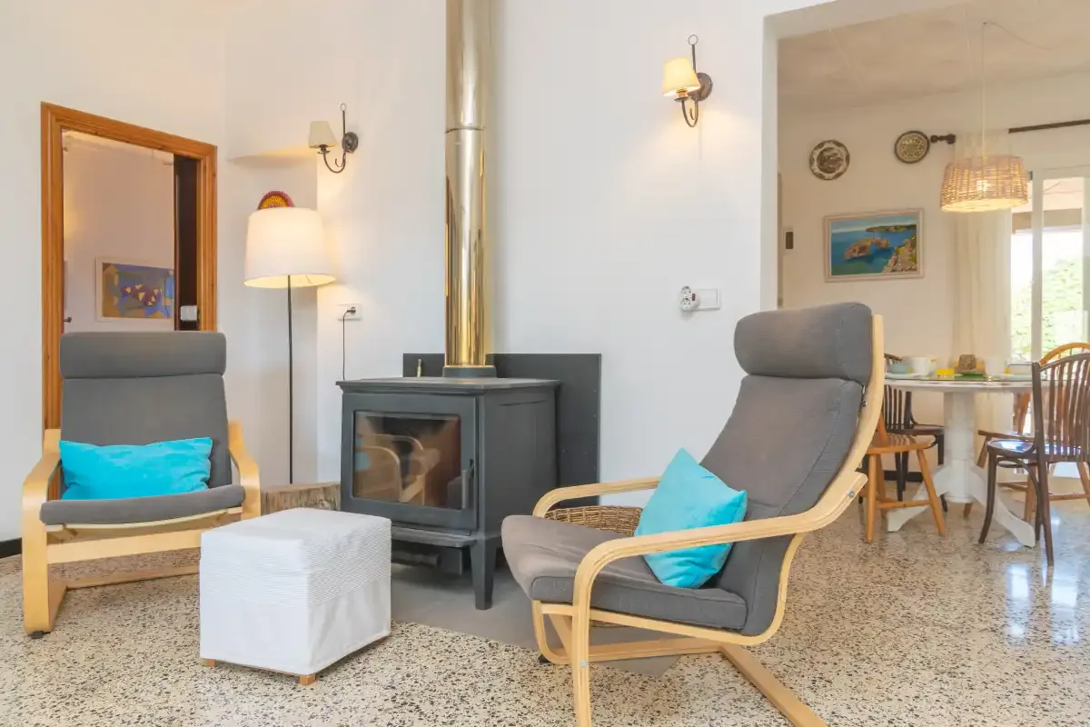 A bright living area has two cushioned seats beside a stove and dining table.