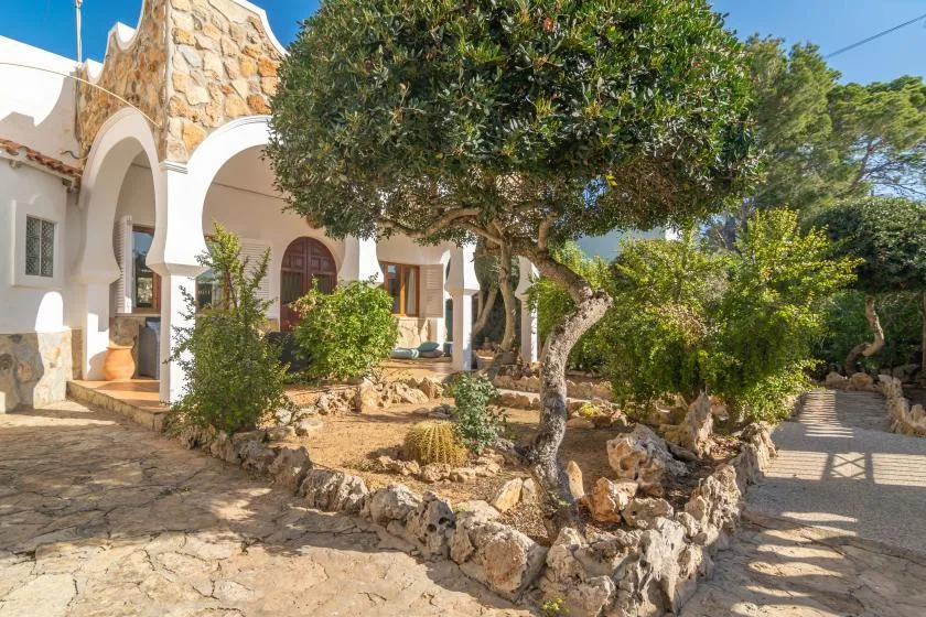 A Mediterranean-style house entrance opens onto a stone courtyard with trees and plants.