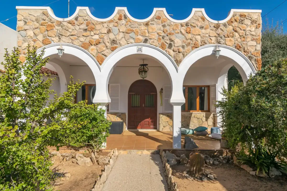 A stone-fronted house has three white arches over its entrance.