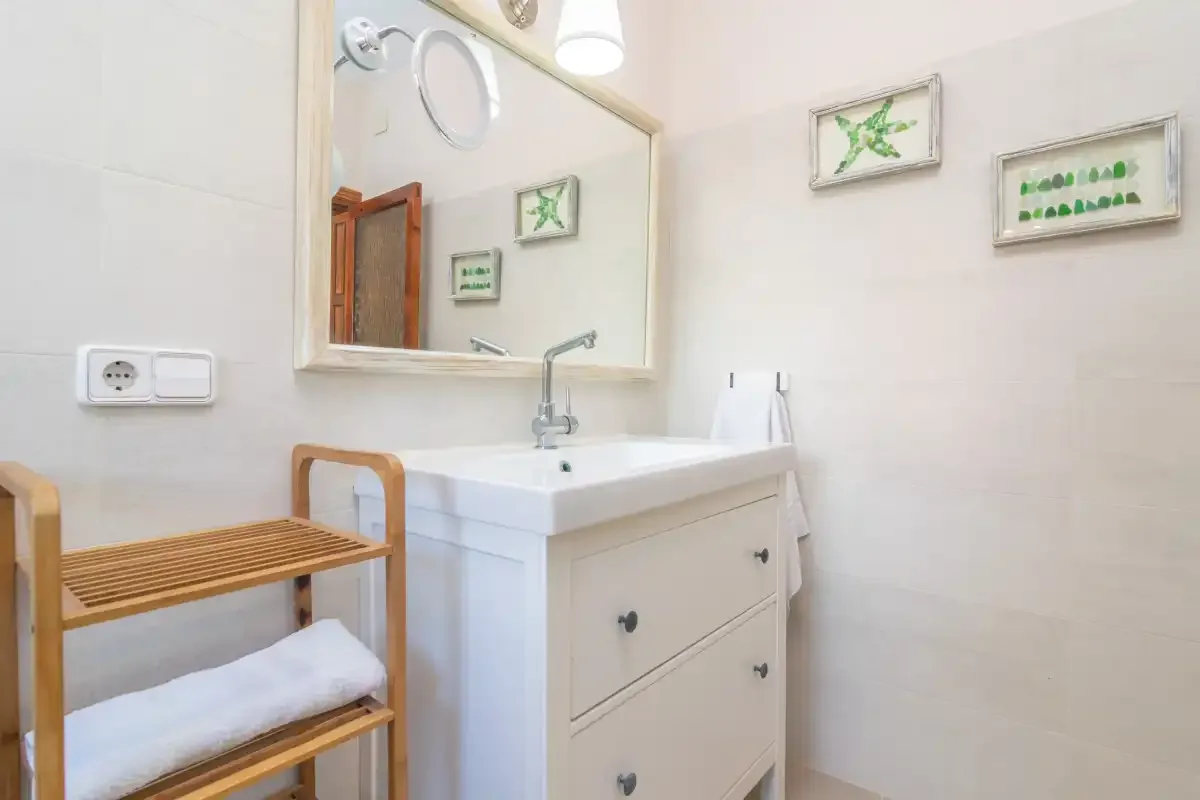 A bright bathroom with a sink, mirror, and wooden bench.