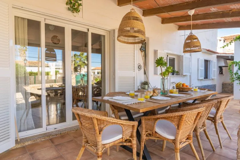 A covered outdoor dining area with a wooden table and woven seating.