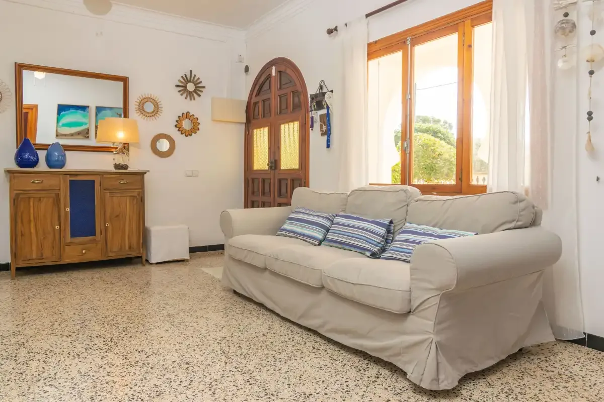 A living room with a sofa and a wooden cabinet beside a bright window.