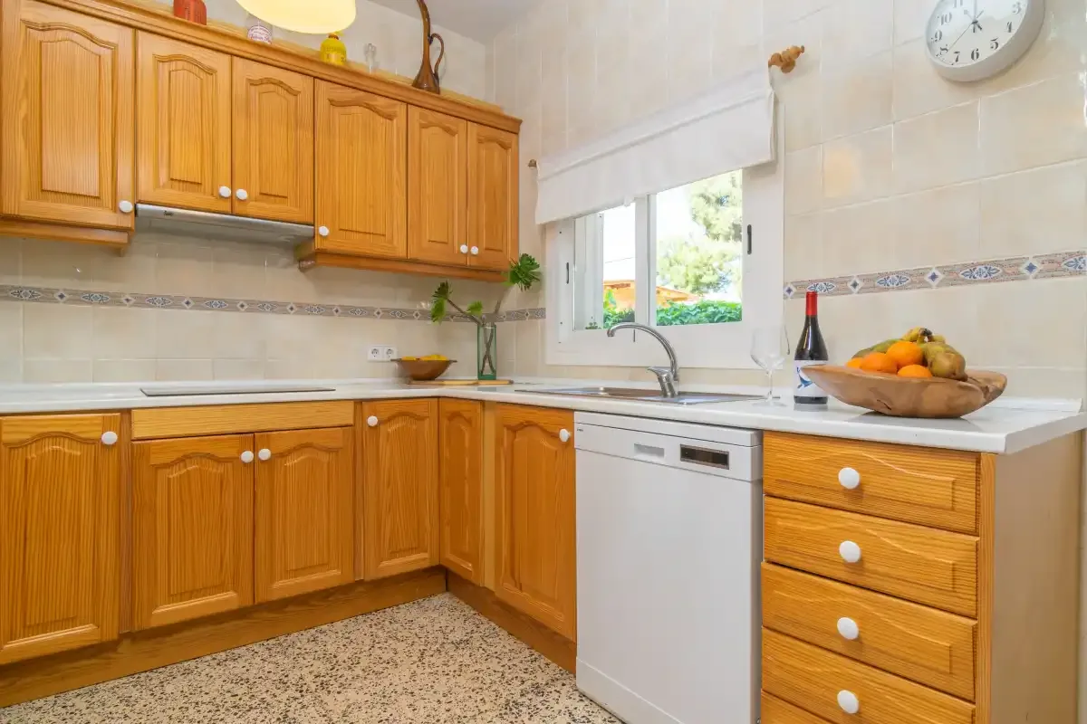 A bright kitchen with wooden cabinets, a dishwasher, and a bowl of fruit.