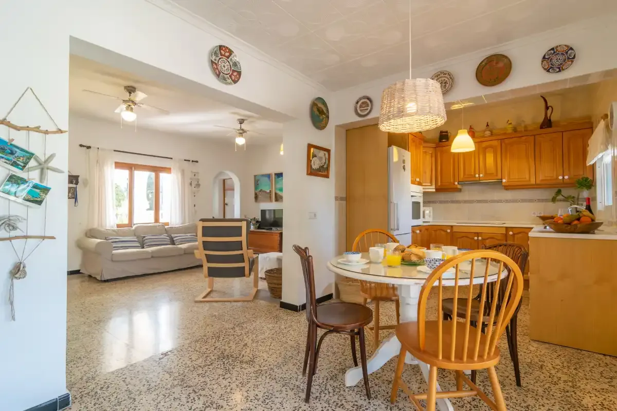 A dining area with a round table and wooden chairs beside an open kitchen.