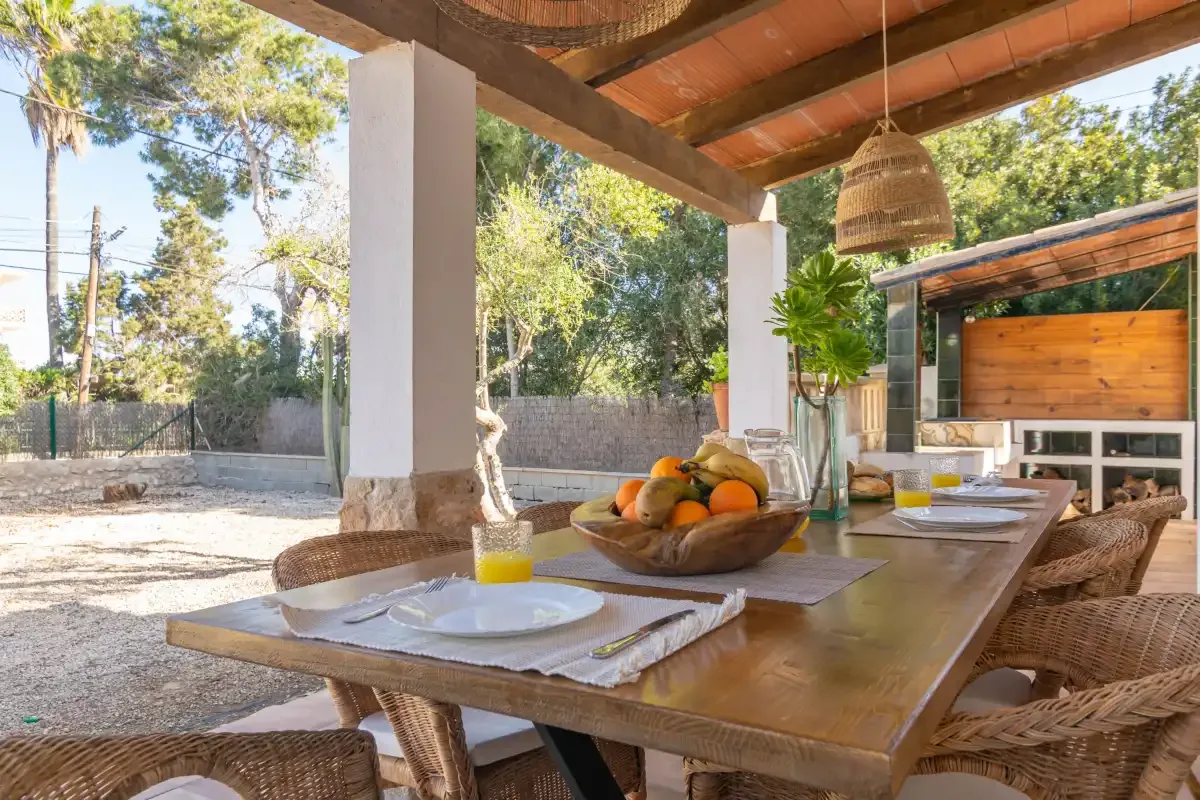 An outdoor dining area with a wooden table set beneath a covered patio.