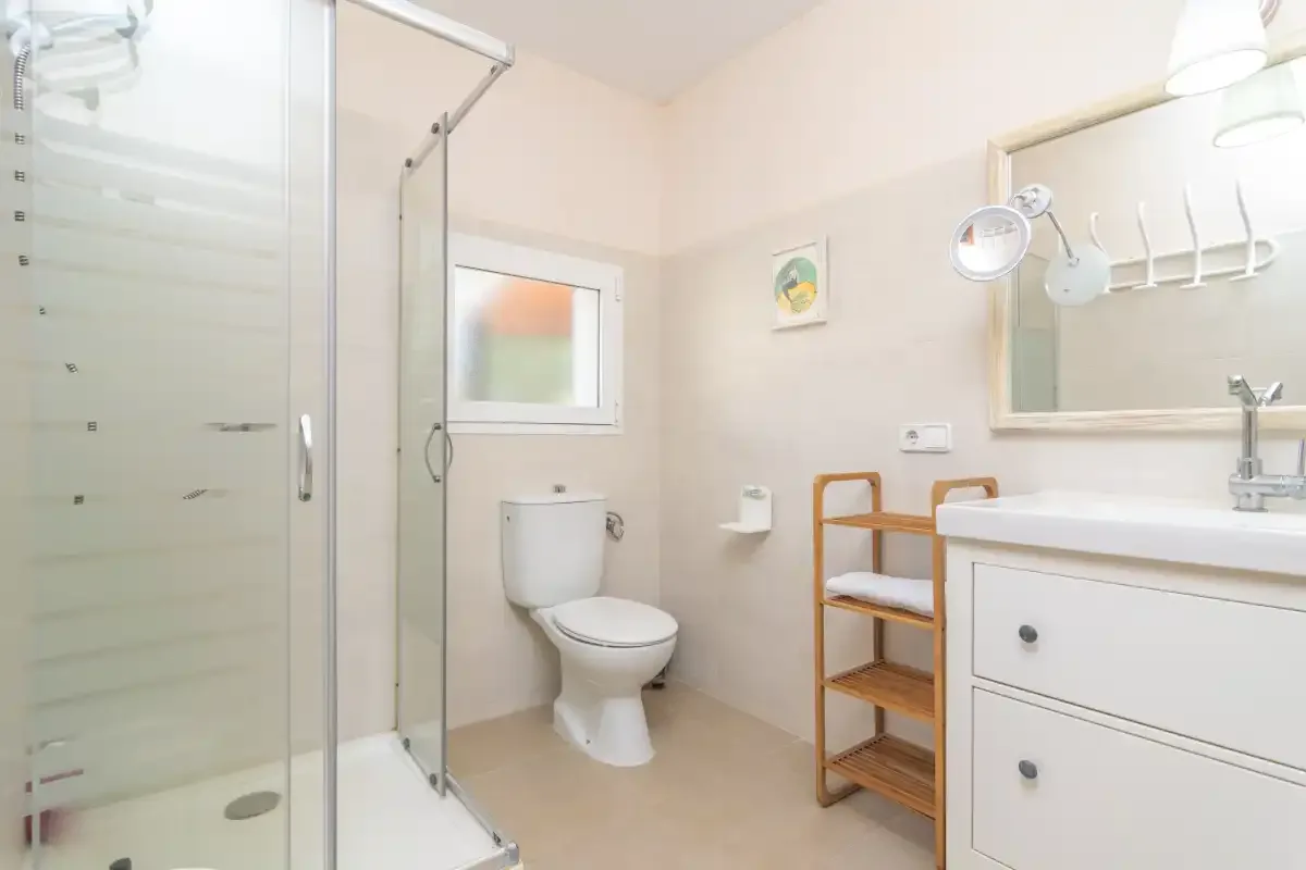 A bright bathroom with a glass shower, toilet, and sink.