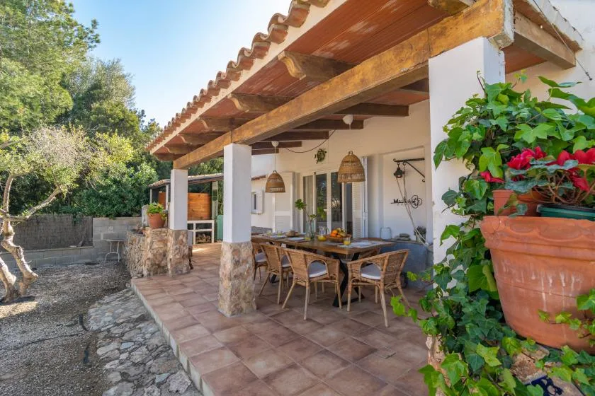 A covered outdoor dining area with a table, seating, and potted plants.