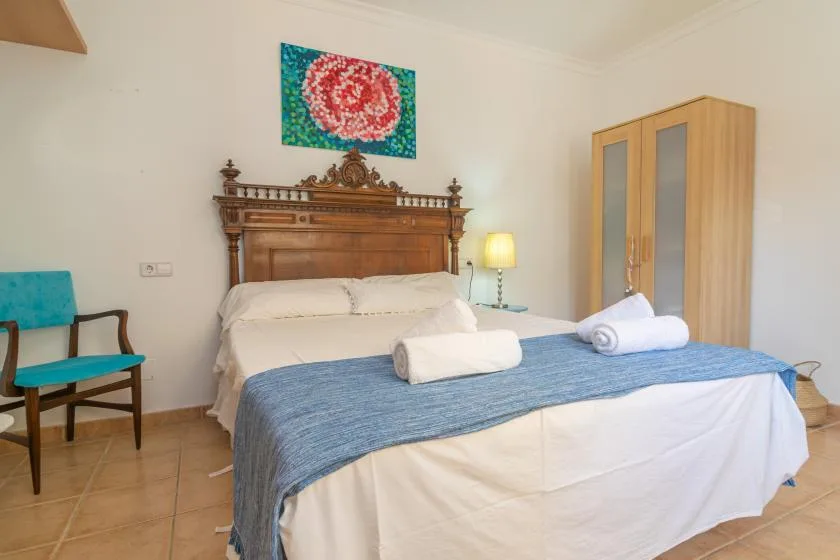 A bedroom with a double bed, blue bedspread, and folded towels.