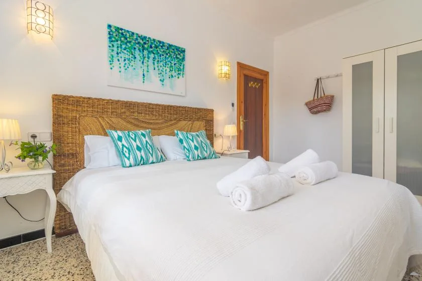 A bedroom with a white bed, patterned pillows, and a woven headboard.