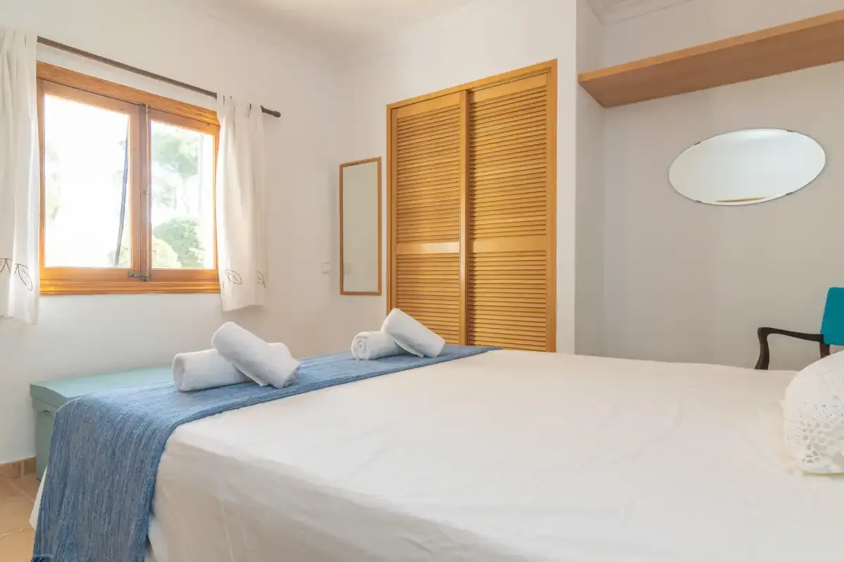 A bedroom with a bed, wooden louvered doors, and a window.