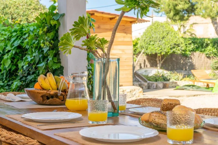An outdoor dining table is set with plates, bread, fruit, and juice.