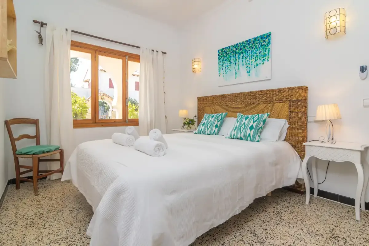 A bedroom with a neatly made bed and a window overlooking greenery.