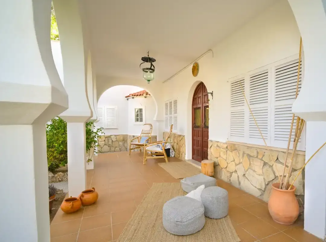A covered patio has arched openings, shuttered windows, and a wooden door.