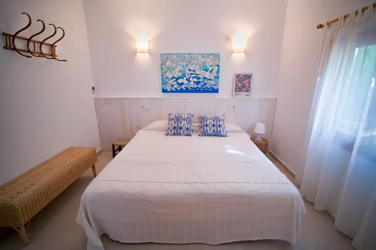A bright bedroom with a neatly made bed and blue artwork above the headboard.