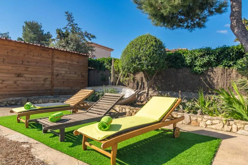 A sunny outdoor lounging area has reclining seats on a patch of green turf.