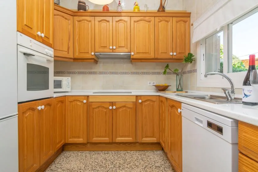 A bright kitchen with wooden cabinets, built-in appliances, and a sink beneath the window.