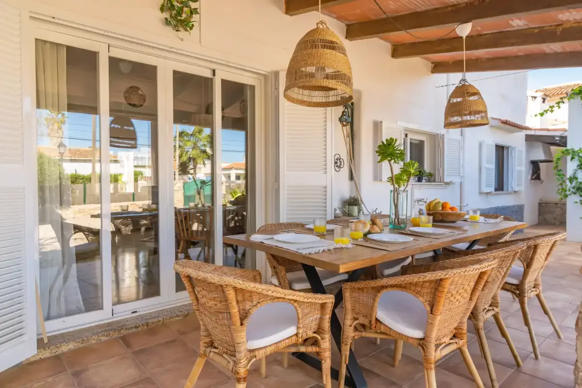 A covered dining patio with a wooden table and wicker seating.