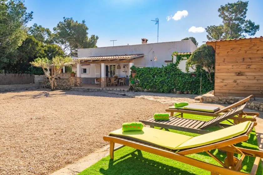 An outdoor patio with reclining loungers faces a single-story house and garden.