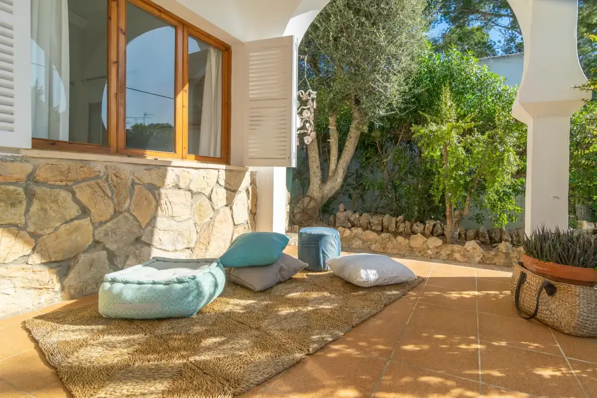 A sunlit patio with floor cushions and leafy trees.