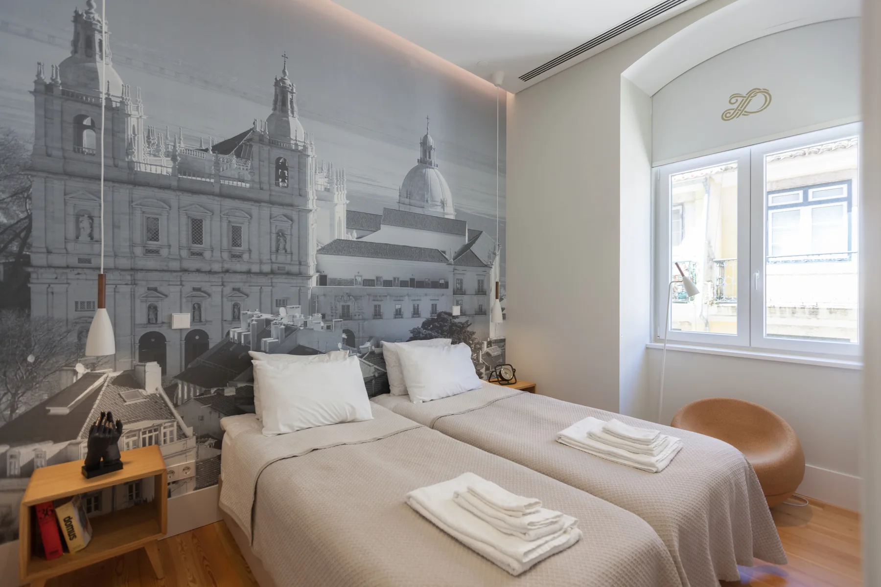 A bedroom with a bed, folded towels, and a large architectural mural.