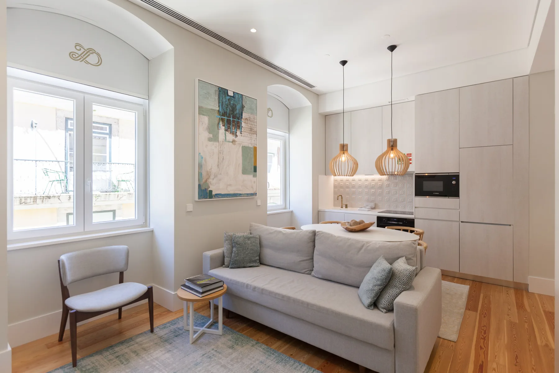 A living room with seating beside a bright window and an open kitchen.