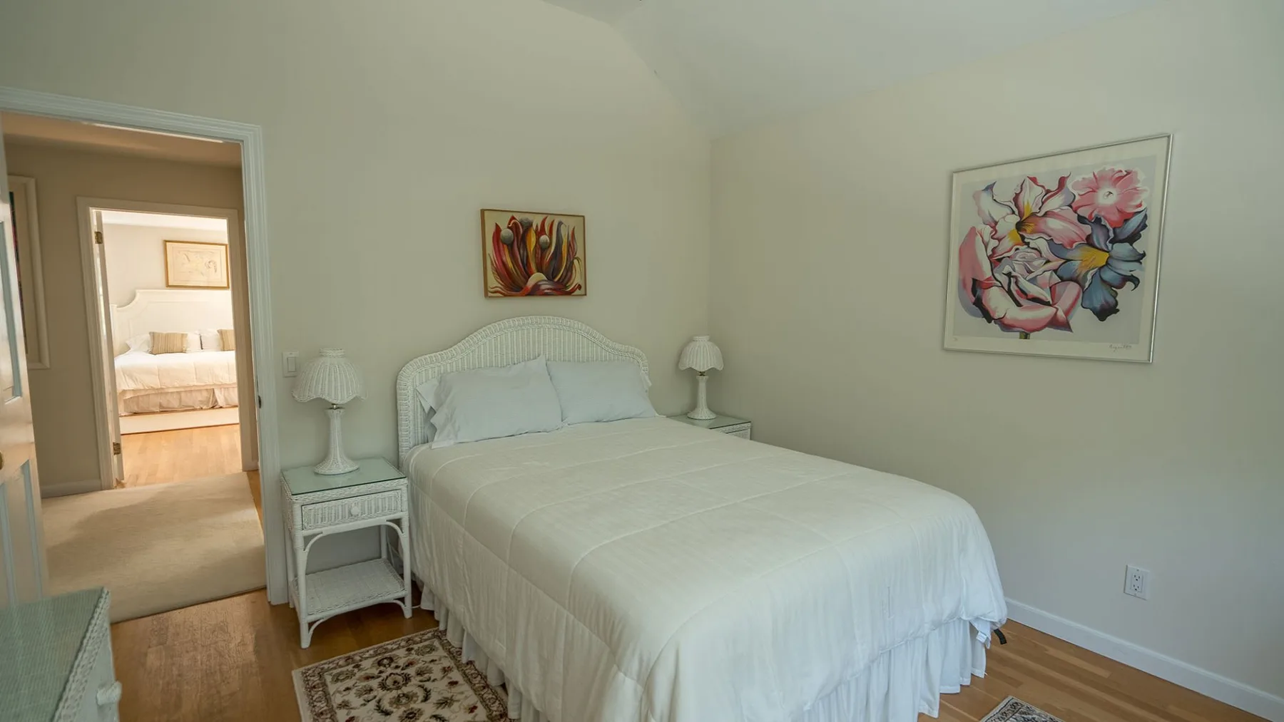 Un dormitorio con una cama bien tendida y cuadros florales enmarcados.