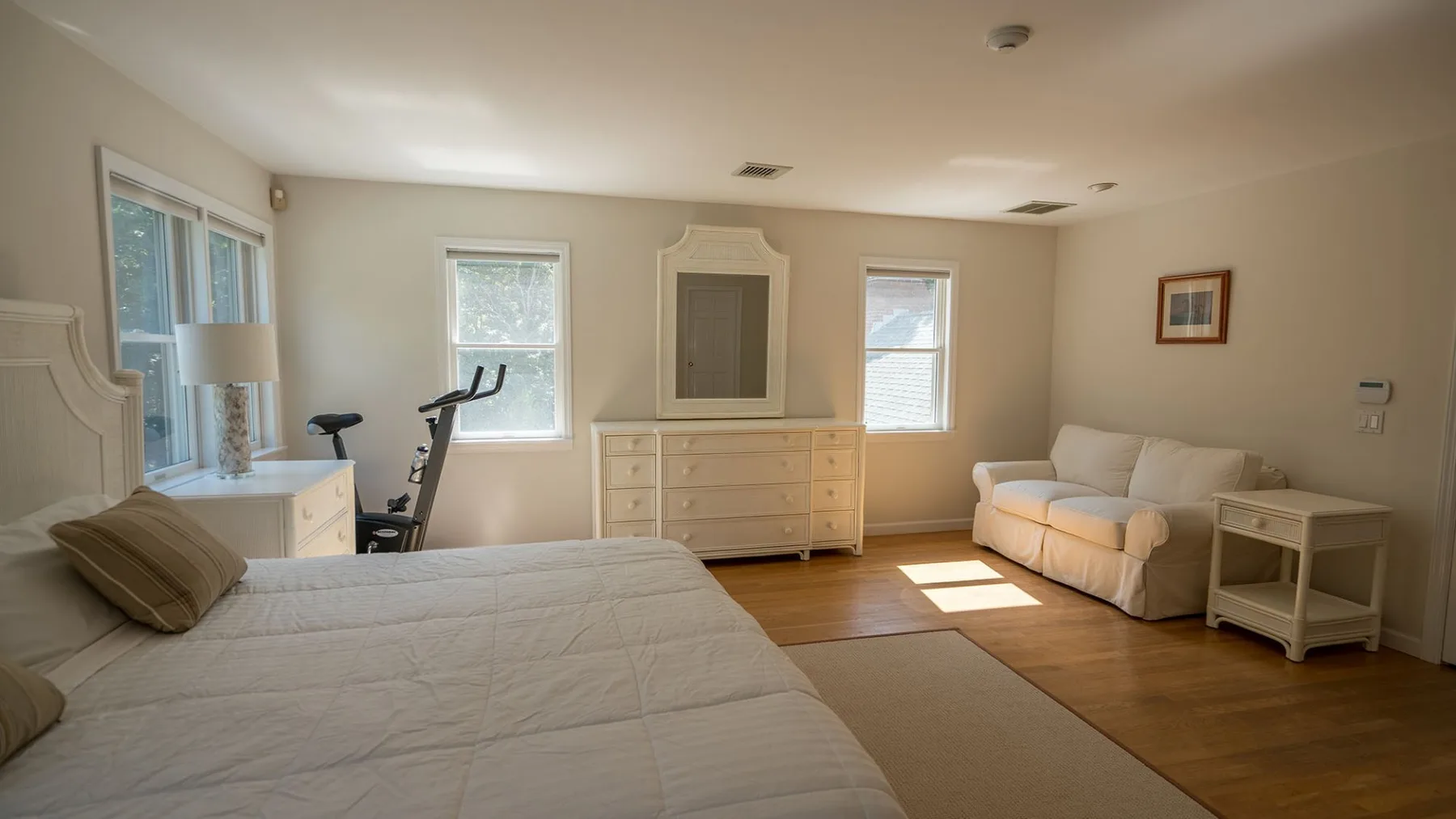 Un dormitorio con una cama grande, una cómoda y una zona de estar junto a las ventanas.