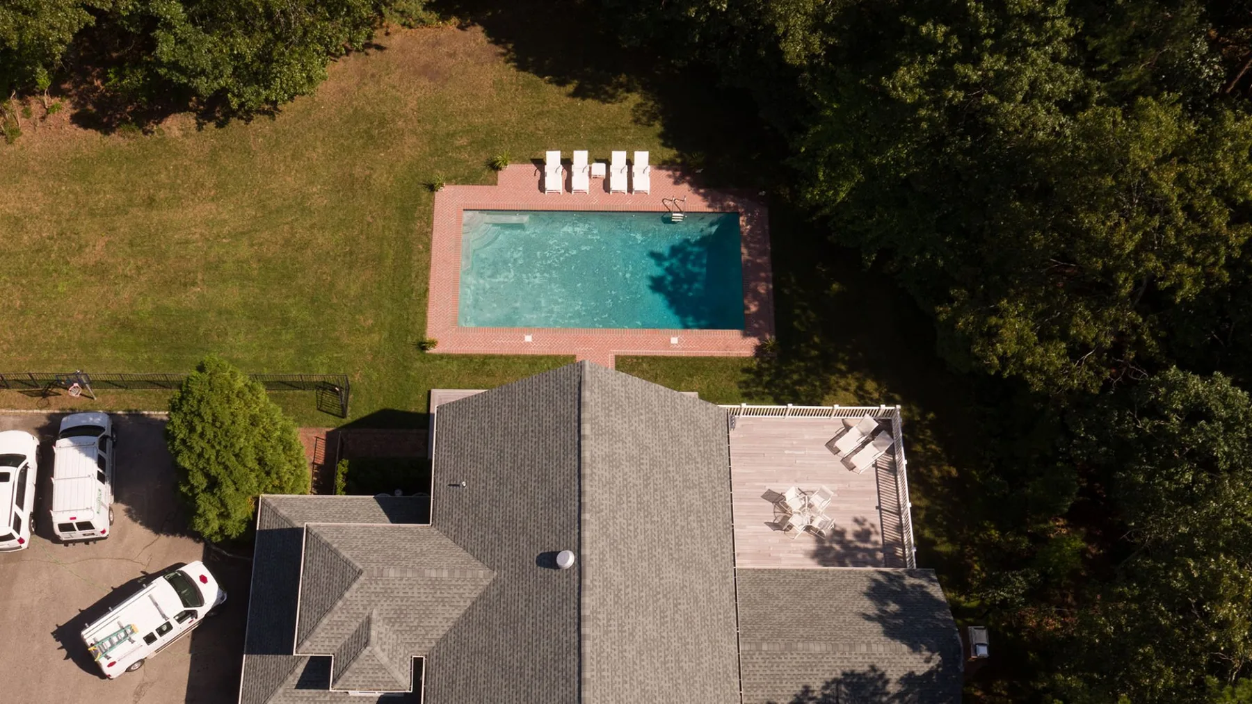 Una vista aérea muestra una casa junto a una piscina rectangular y una zona de estacionamiento pavimentada.