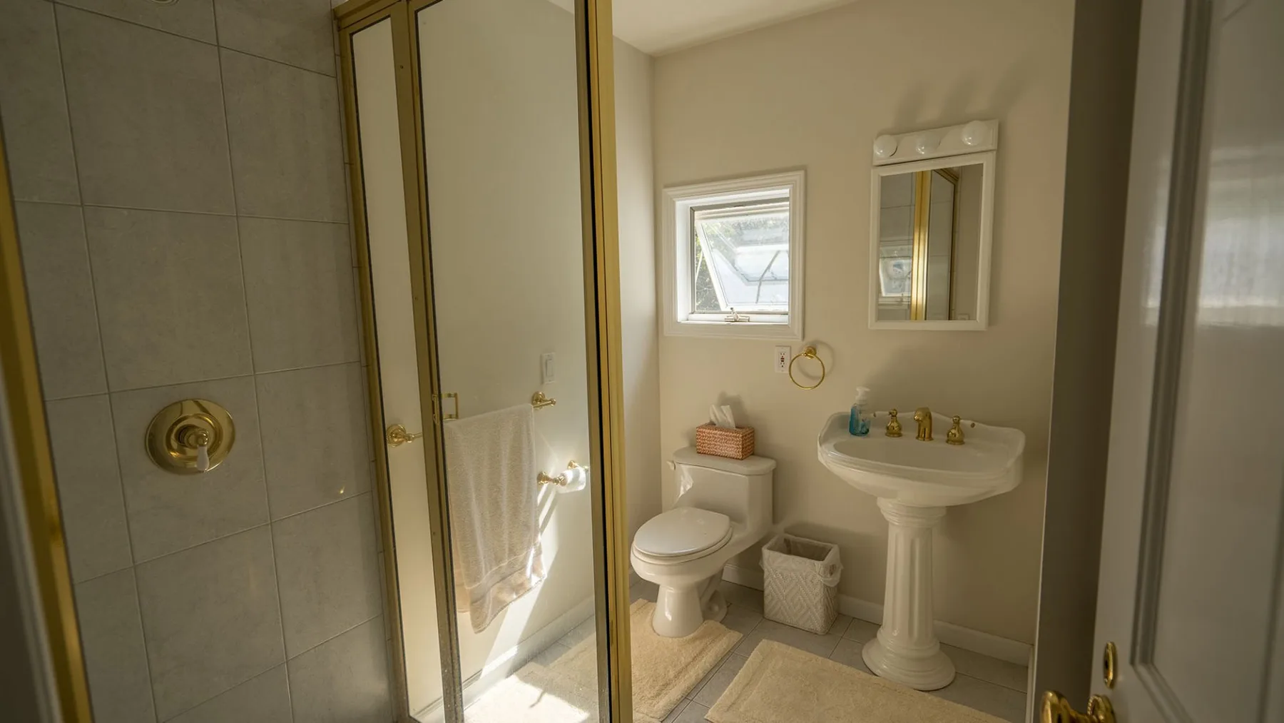 Un baño con ducha, inodoro, lavabo de pedestal y ventana.