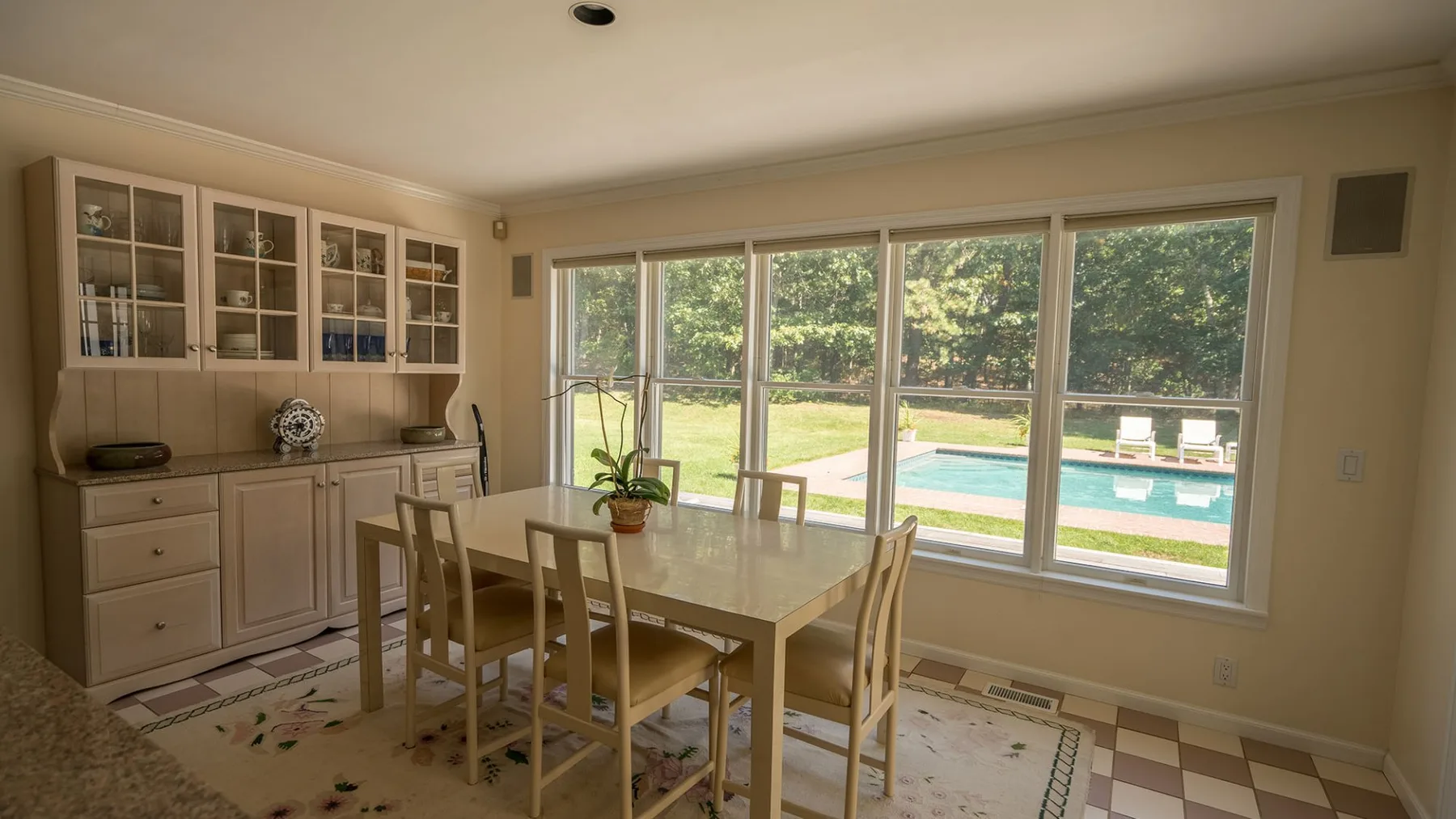 Comedor con una mesa y sillas junto a grandes ventanas con vistas a una piscina.