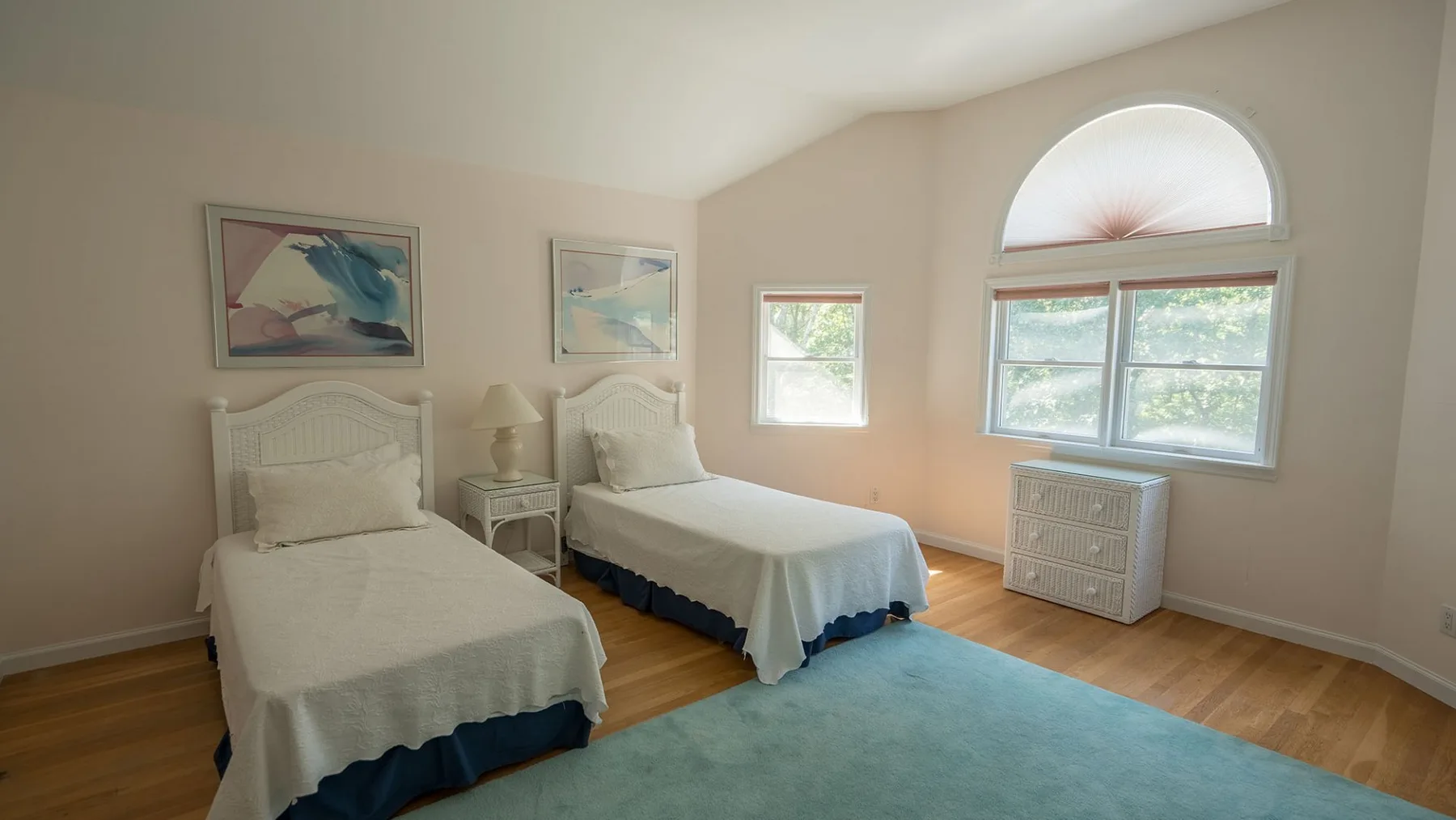 Un dormitorio luminoso con dos camas, cuadros enmarcados y ventanas grandes.