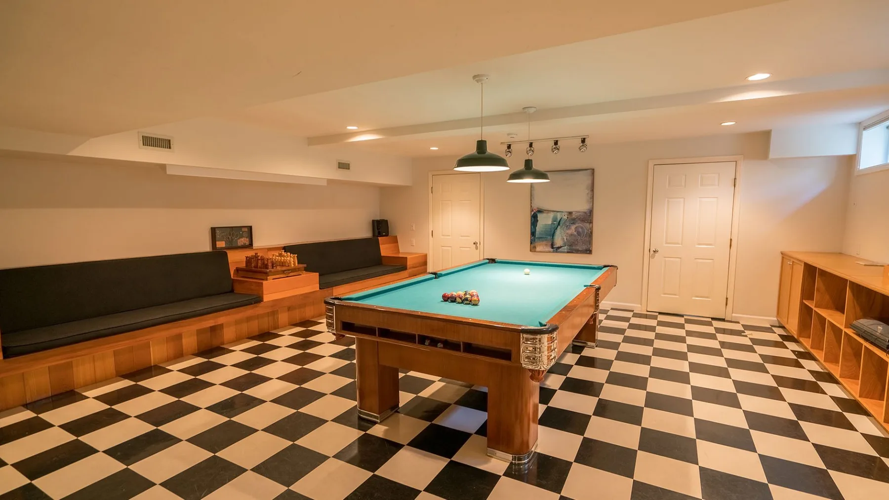 Una sala de juegos cuenta con una mesa de billar y asientos largos junto a la pared.