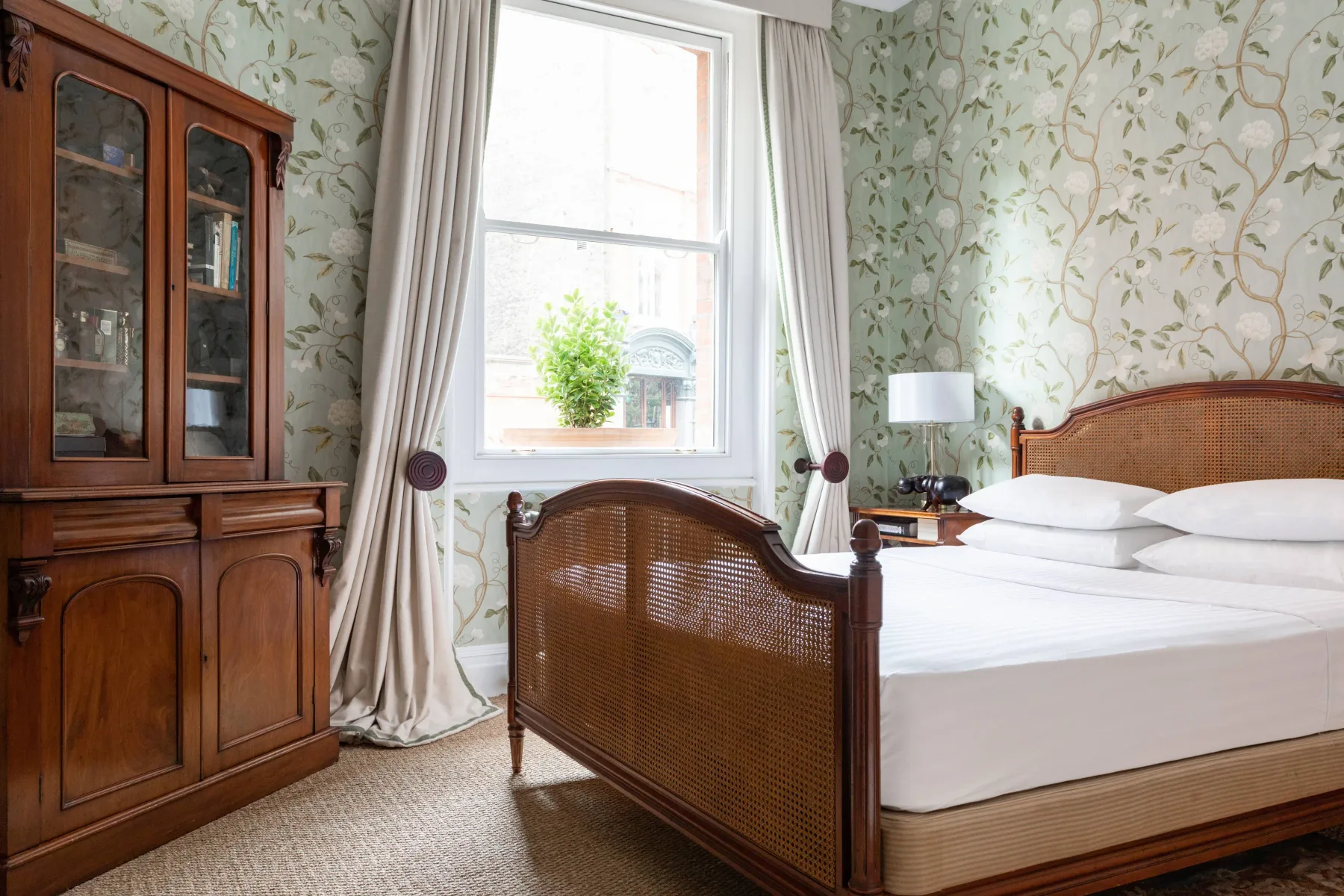 A bedroom with a woven bed, wooden cabinet, and bright window.