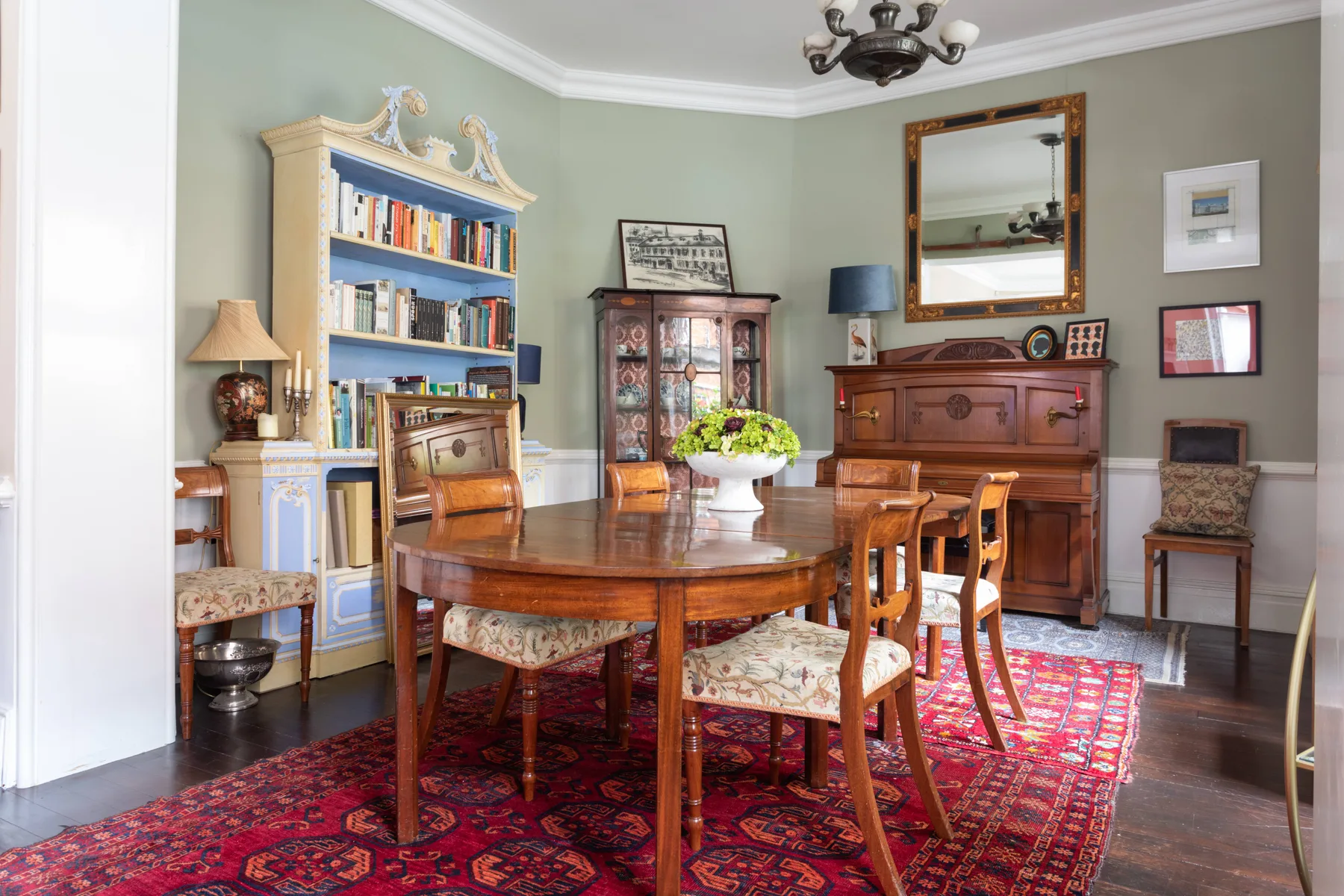 A dining room with a wooden table, chairs, and a patterned rug.