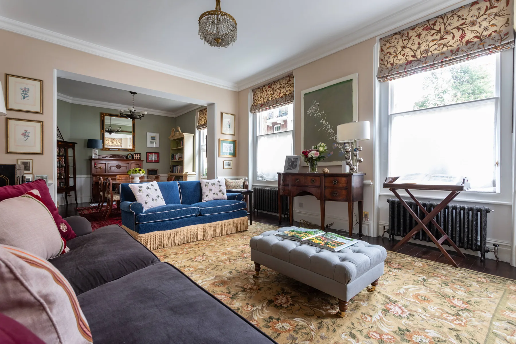 A sitting room with blue seating, a floral rug, and large windows.