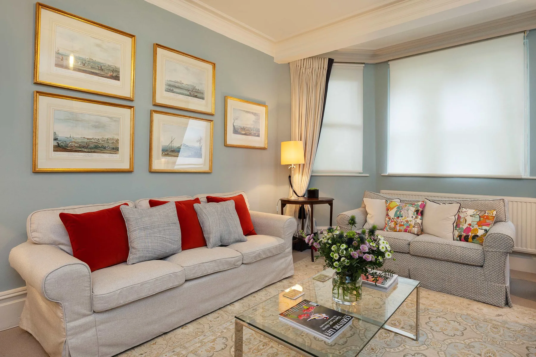 A living room with seating, framed artwork, and a glass coffee table.
